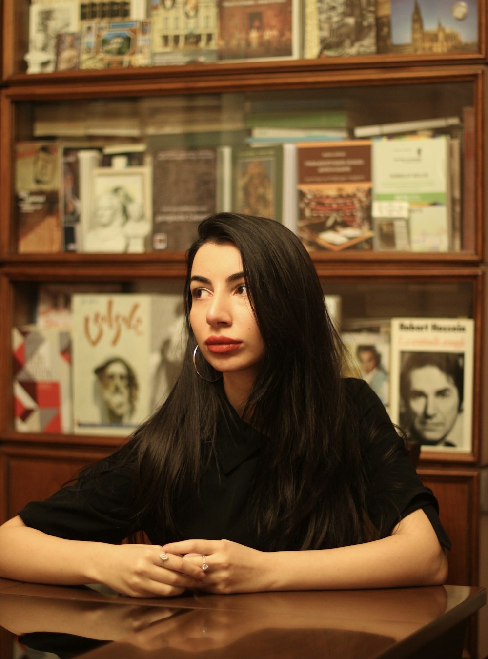 a woman sitting at a table in front of a book shelf