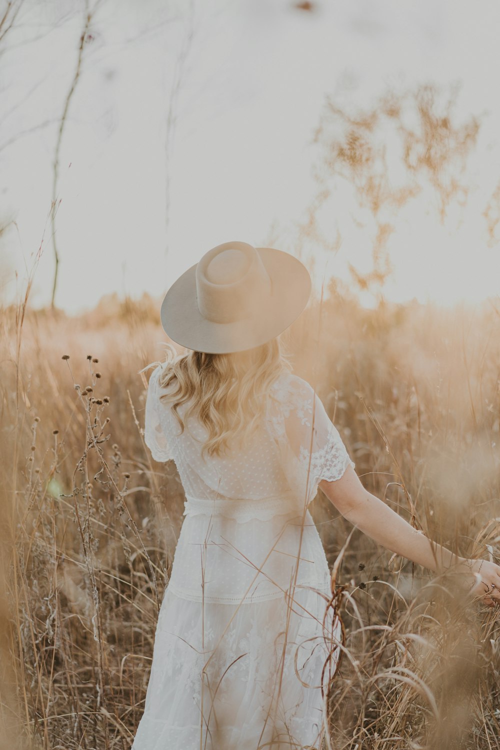 a woman in a white dress and hat walking through tall grass