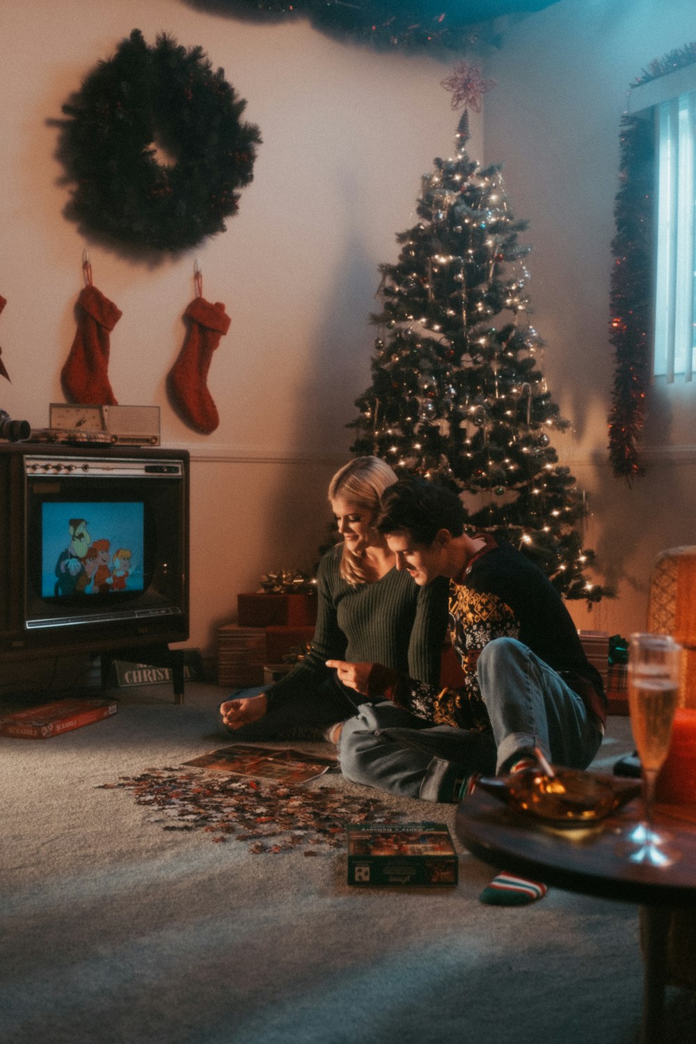 two people sitting on the floor in front of a christmas tree