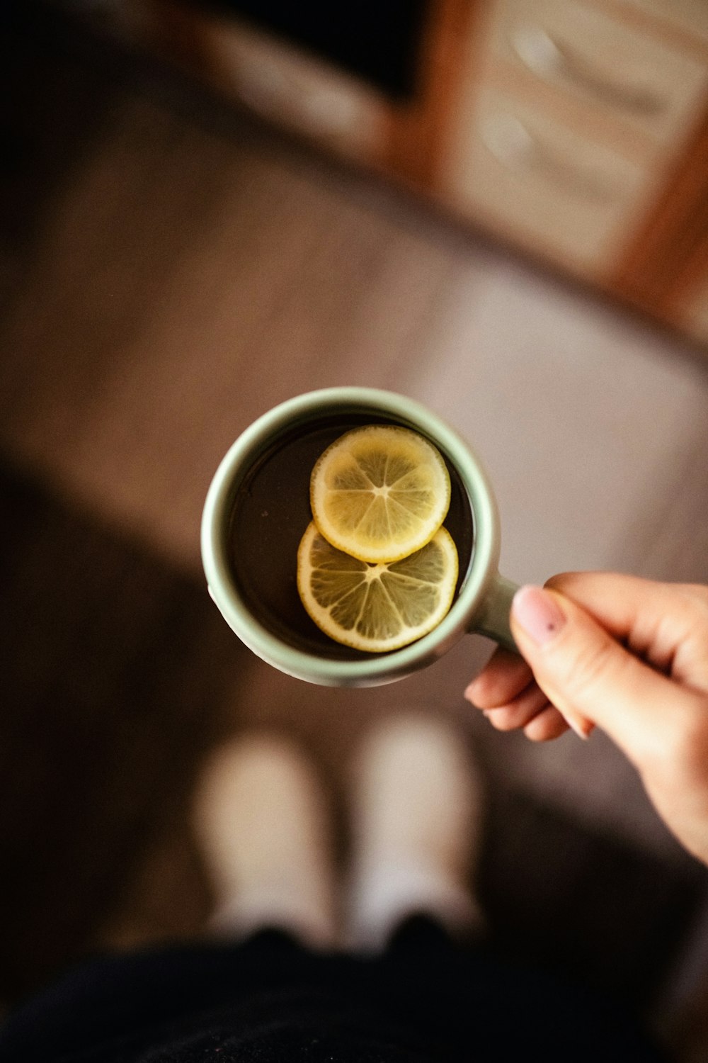 a person holding a cup of tea with lemon slices in it