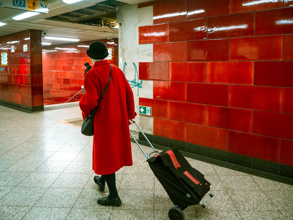 a woman in a red coat pulling a black suitcase