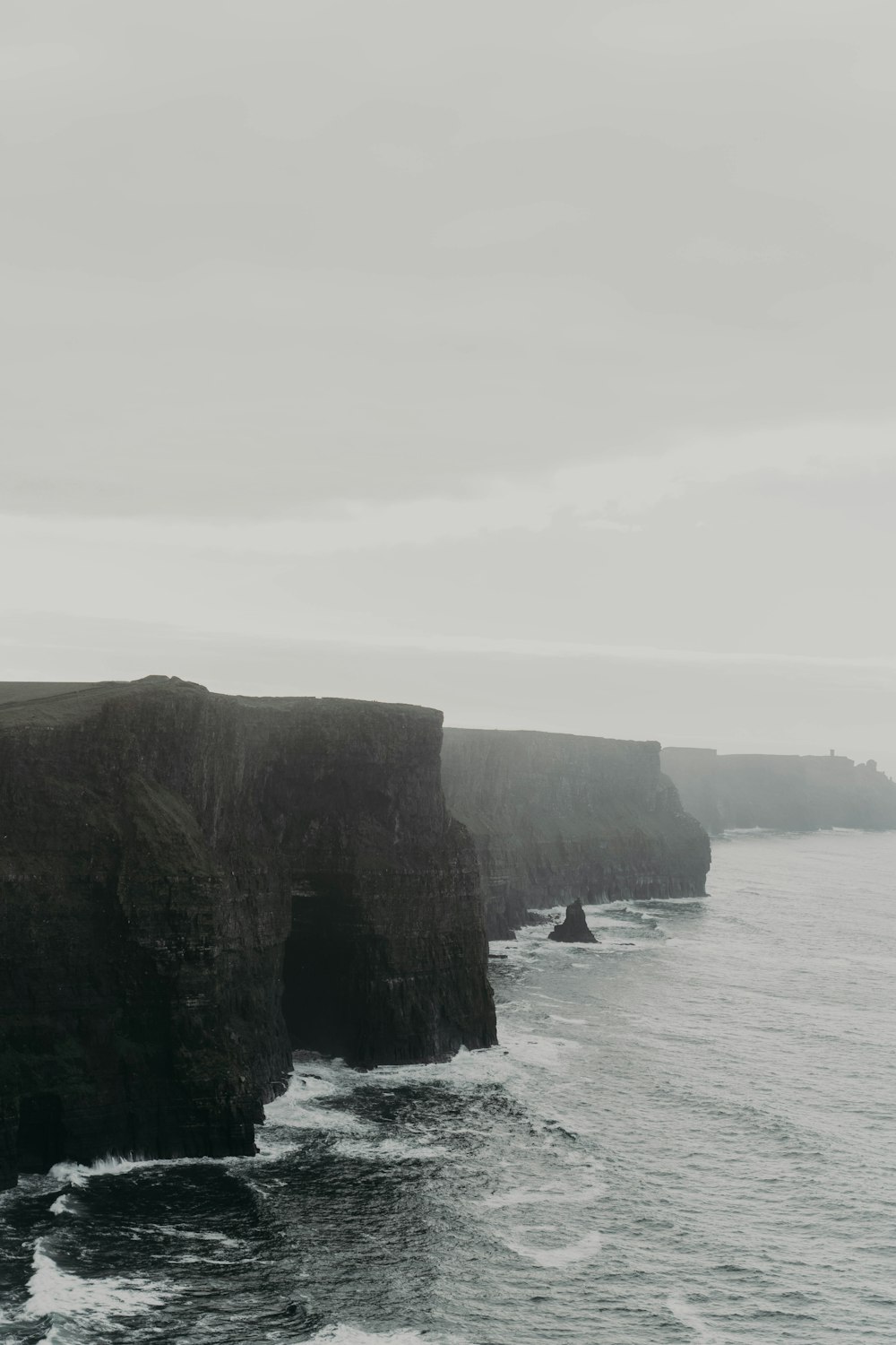 a black and white photo of a cliff by the ocean