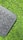 A section of a black keyboard with circular keys rests on a surface of vibrant green artificial grass. The keys visible include function keys, enter, shift, and a deletion key.