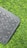 A section of a black keyboard with circular keys rests on a surface of vibrant green artificial grass. The keys visible include function keys, enter, shift, and a deletion key.