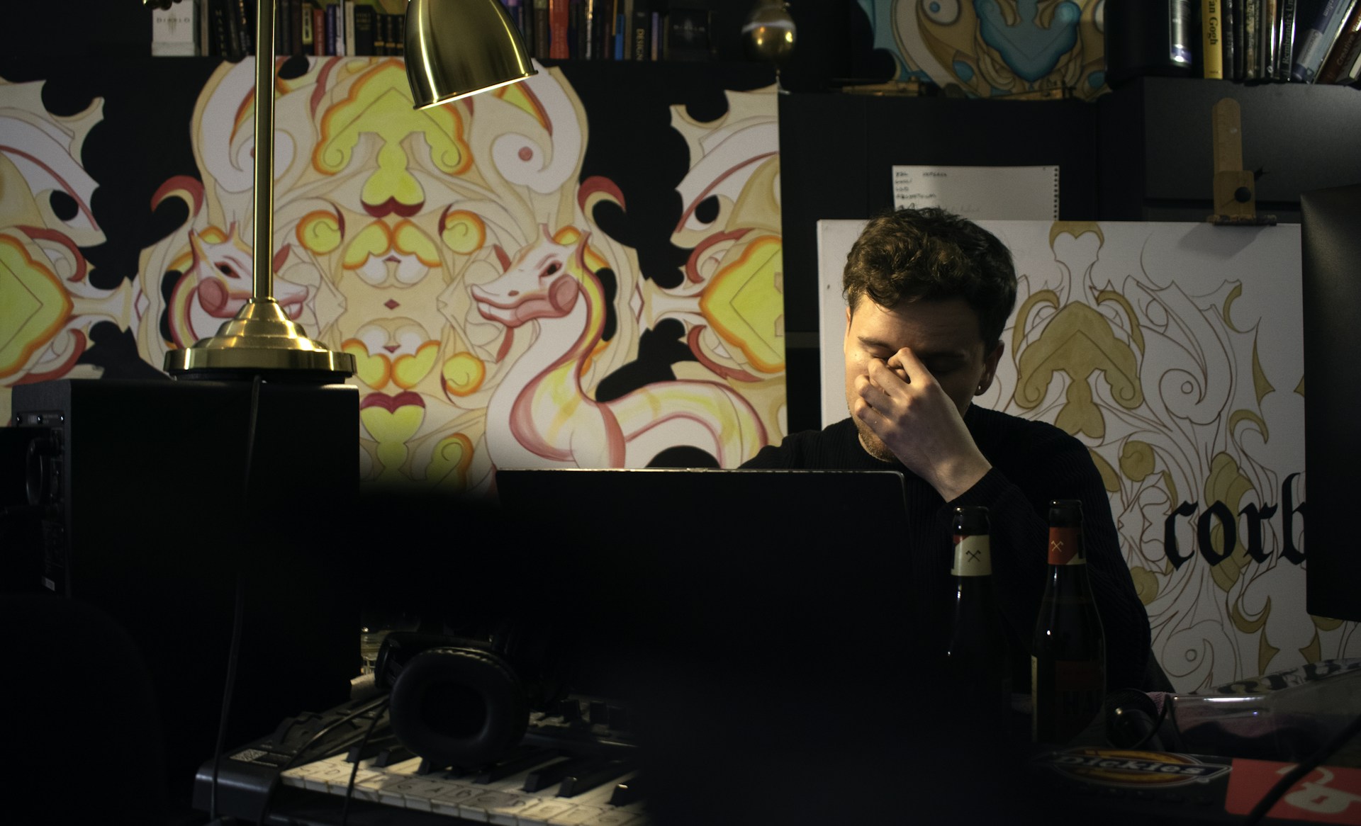 A candid shot of a man thoughtfully working at his desk, surrounded by personal mementos and a laptop.