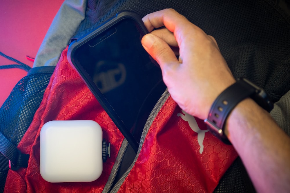 uma pessoa segurando um smartphone ao lado de uma mochila