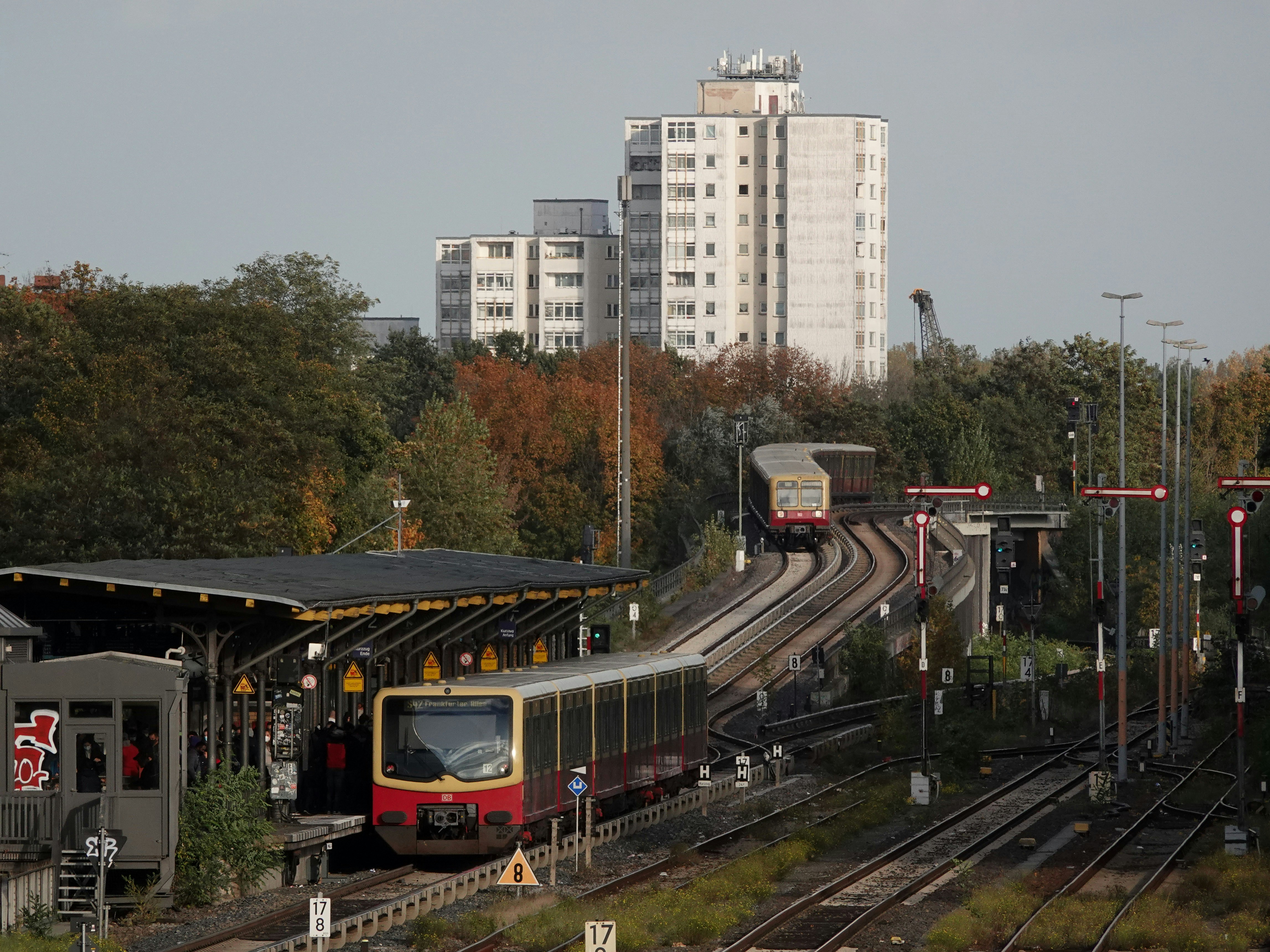 a train traveling down train tracks next to tall buildings, S-Bahn Station Neukölln