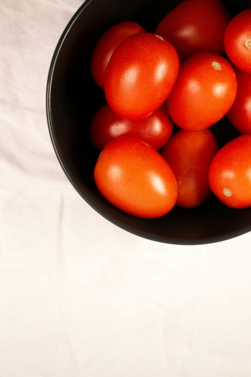 a black bowl filled with lots of ripe tomatoes