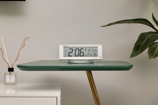 a clock sitting on top of a table next to a plant