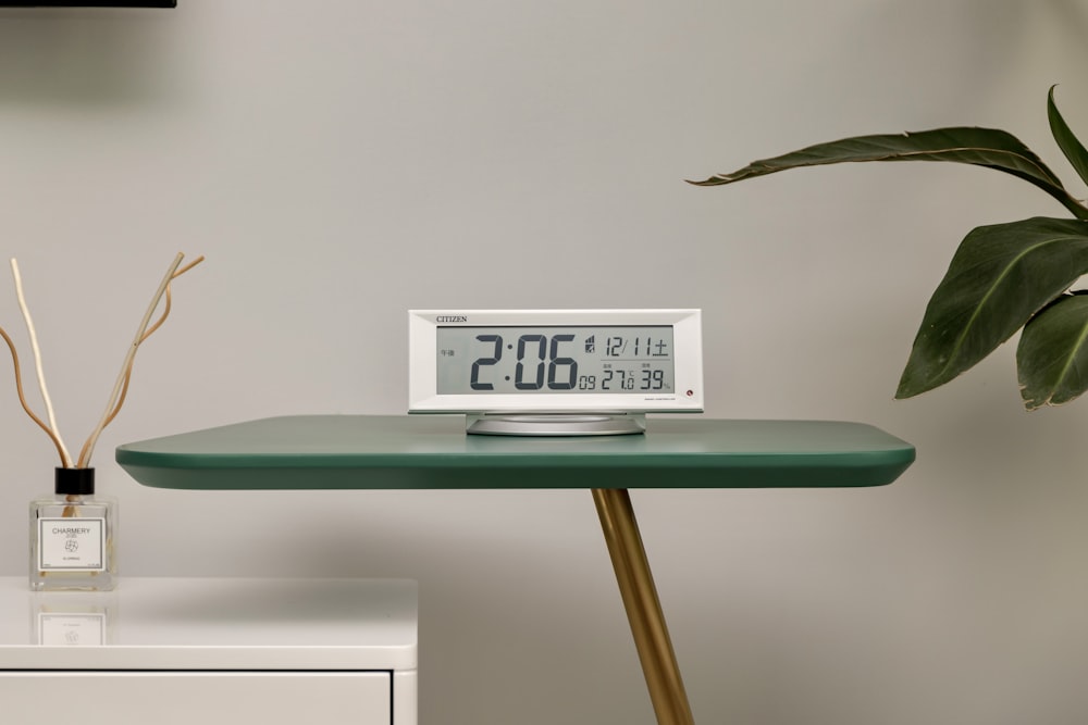 a clock sitting on top of a table next to a plant