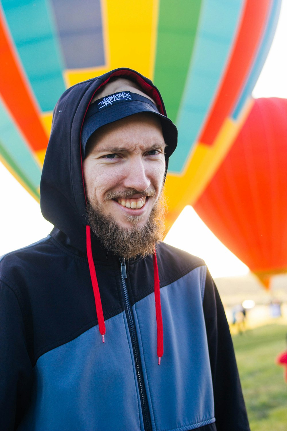 a man with a beard and a hoodie standing in front of hot air balloons