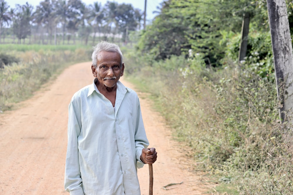a man standing on a dirt road holding a stick