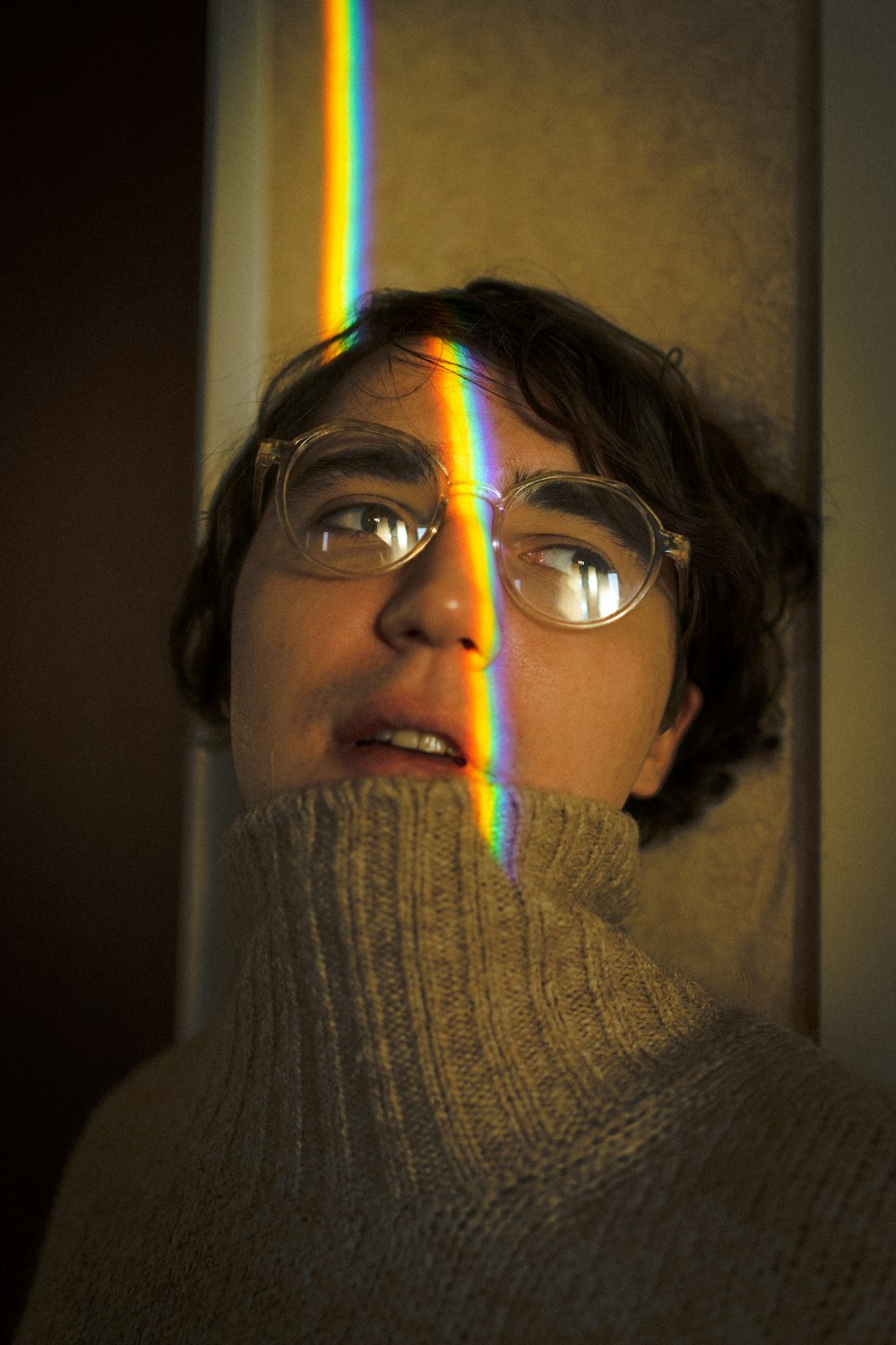 a man wearing glasses and a sweater with a rainbow in the background