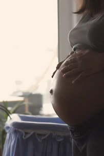 a pregnant woman holding her stomach in front of a window at 2Ls in Bowmanville. Prenatal Massage