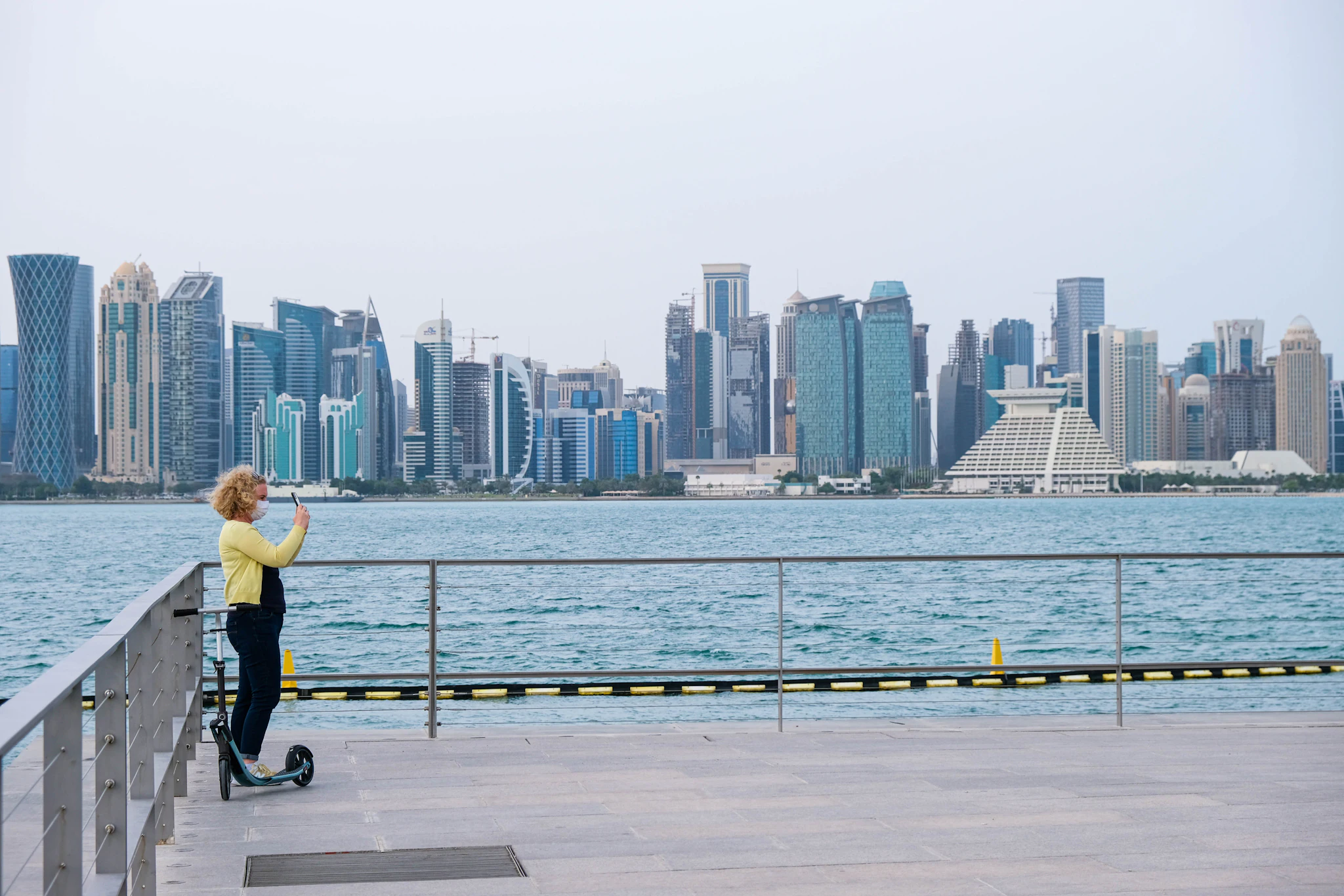 A woman on a scooter looking across the water at the Doha skyline
