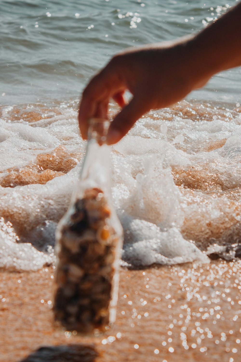 a person reaching for a bottle on the beach