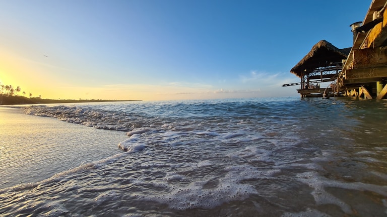 Golden sunset over a serene beach in the Maldives, with luxury villas glowing warmly.