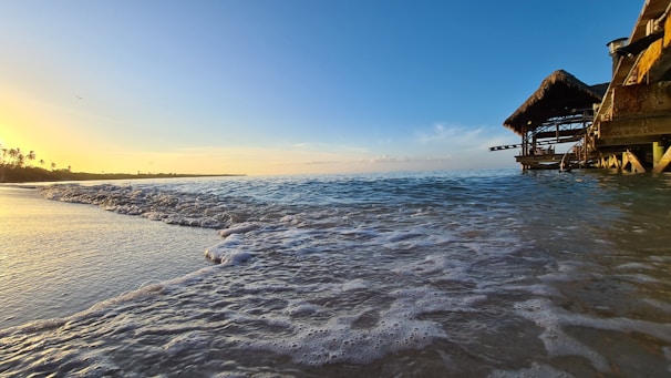 A cozy beachfront bungalow at sunset with soft golden light reflecting on the waves.