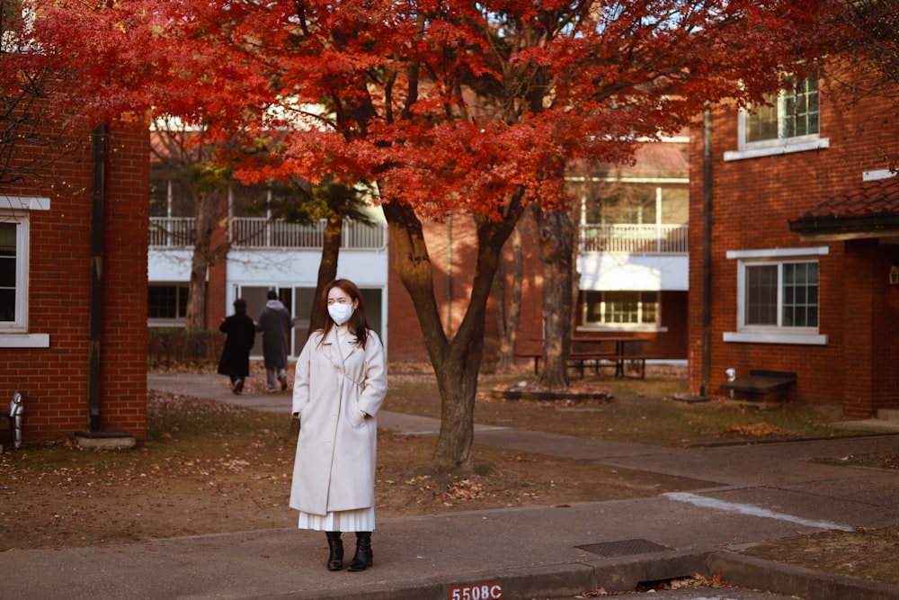a woman wearing a face mask standing in front of a tree