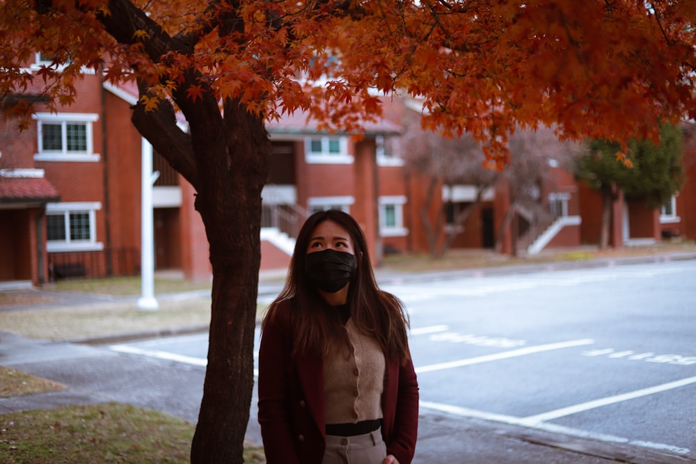 a woman wearing a face mask standing in front of a tree