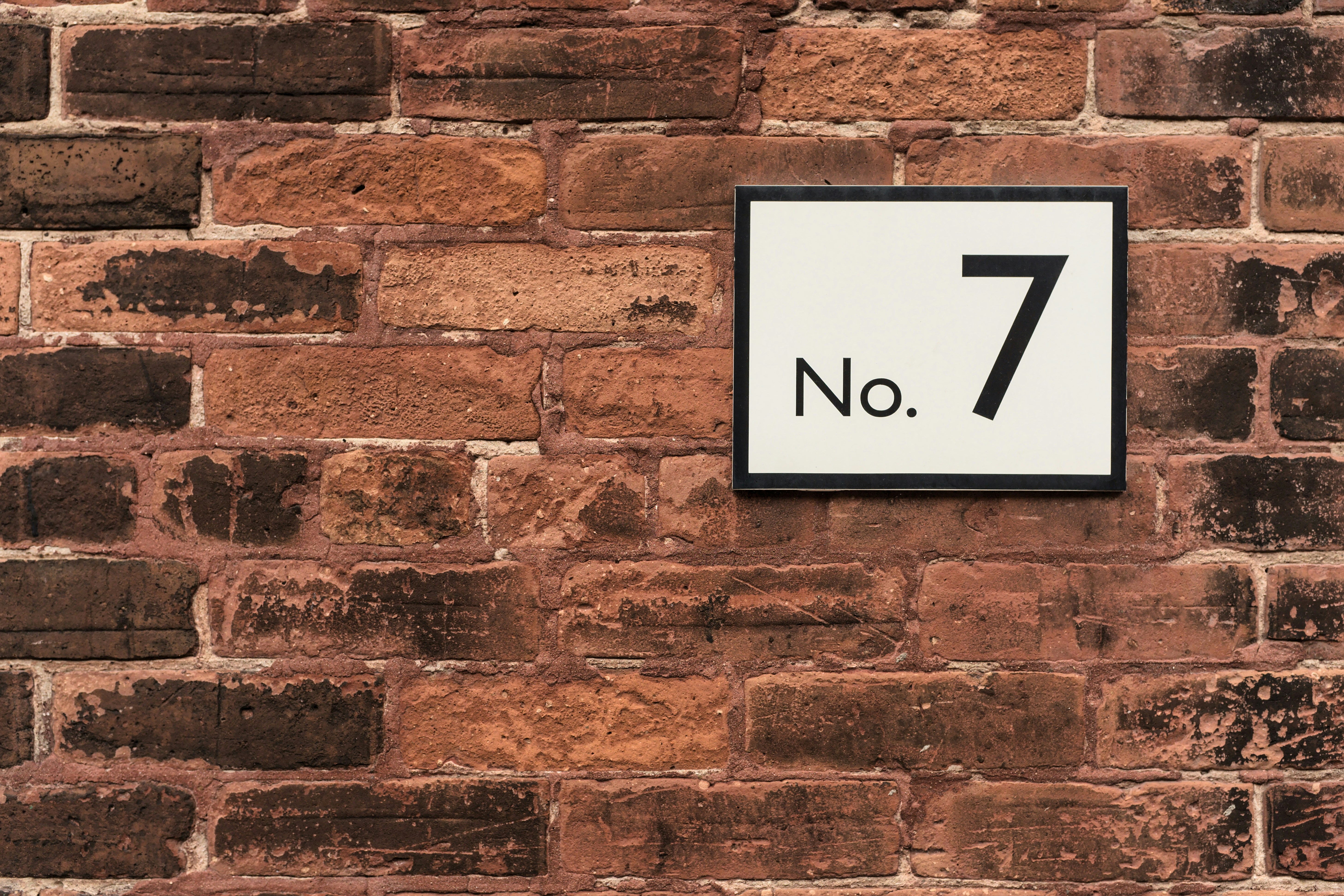 Black and White Number Seven Sign on Red Brick Wall - A black and white sign with the number seven and the word No. is mounted on a red brick wall.