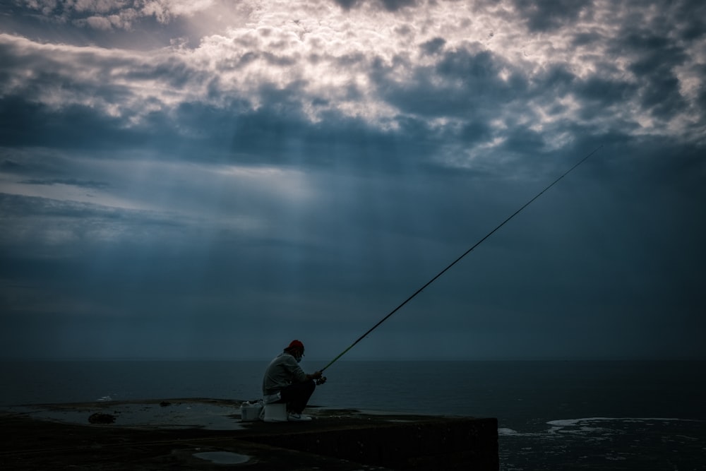 a man sitting on a pier fishing on a cloudy day