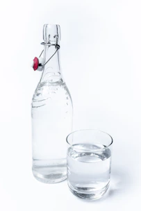 Close-up of a glass bottle filled with clear Zam Zam water, set against a white background with emerald green and gold accents.