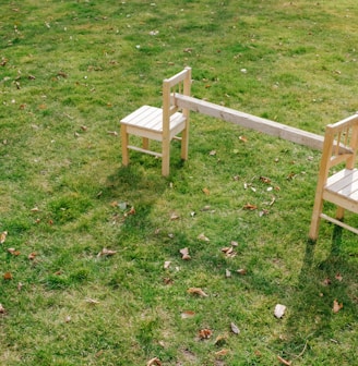 a couple of wooden chairs sitting on top of a lush green field