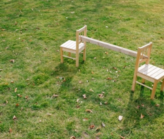 a couple of wooden chairs sitting on top of a lush green field