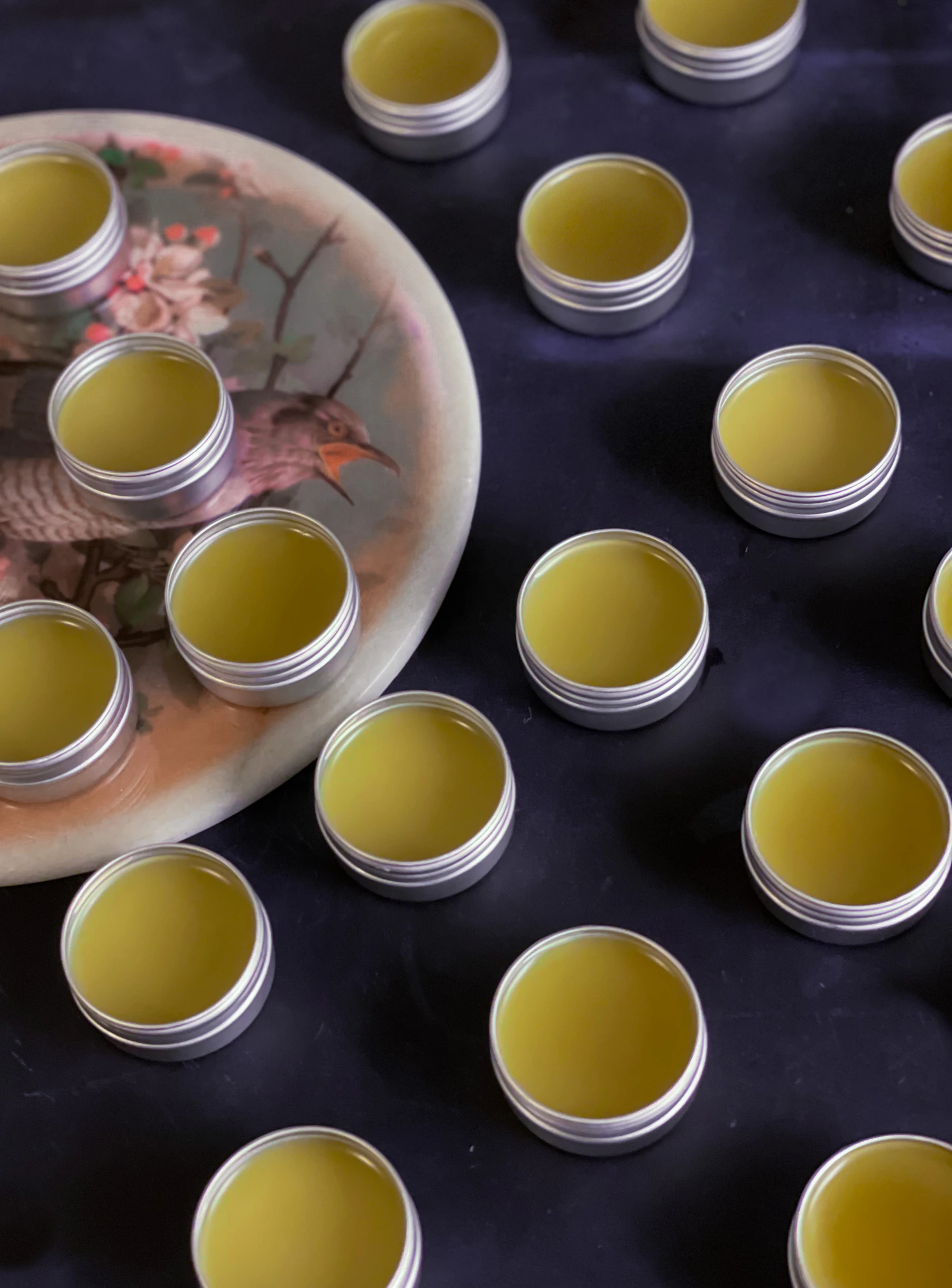 Open round tins of set yellow-green salve laid out on a dark cloth