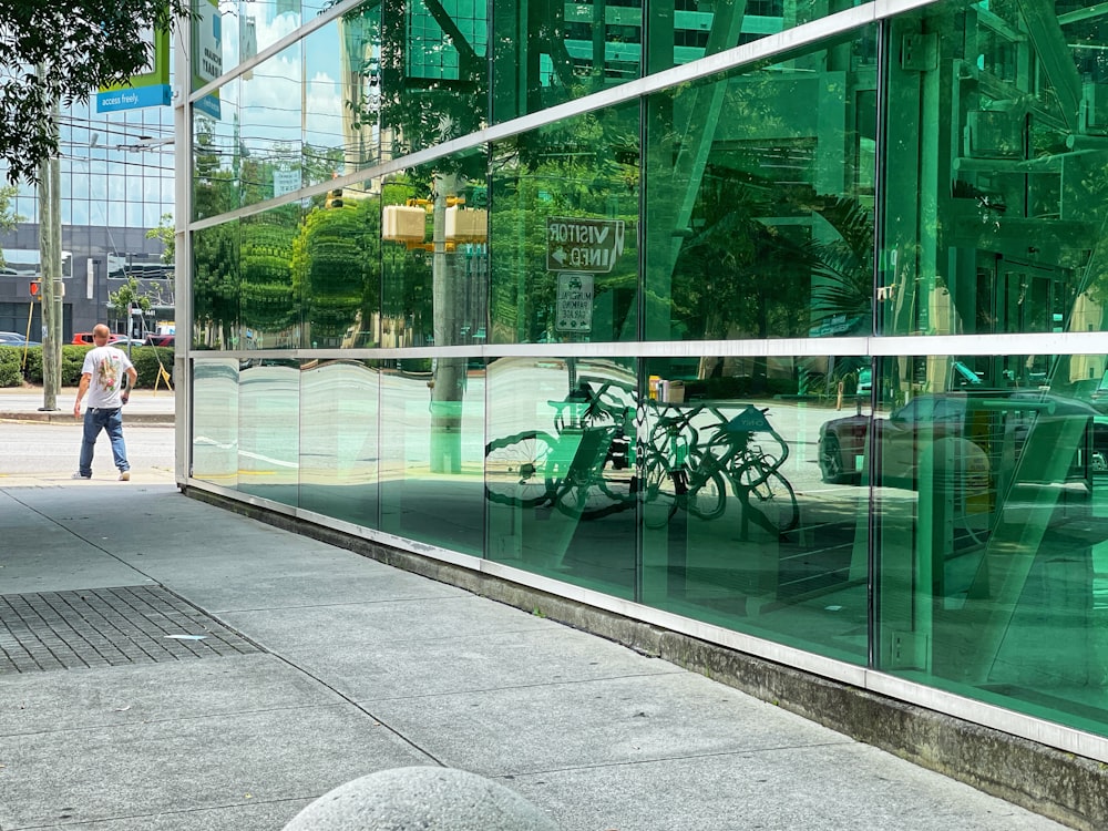 a man walking down a sidewalk past a glass building