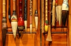A collection of traditional calligraphy brushes hangs against a wooden wall. These brushes come in various sizes and designs, showcasing intricate craftsmanship with decorative elements on the handles.