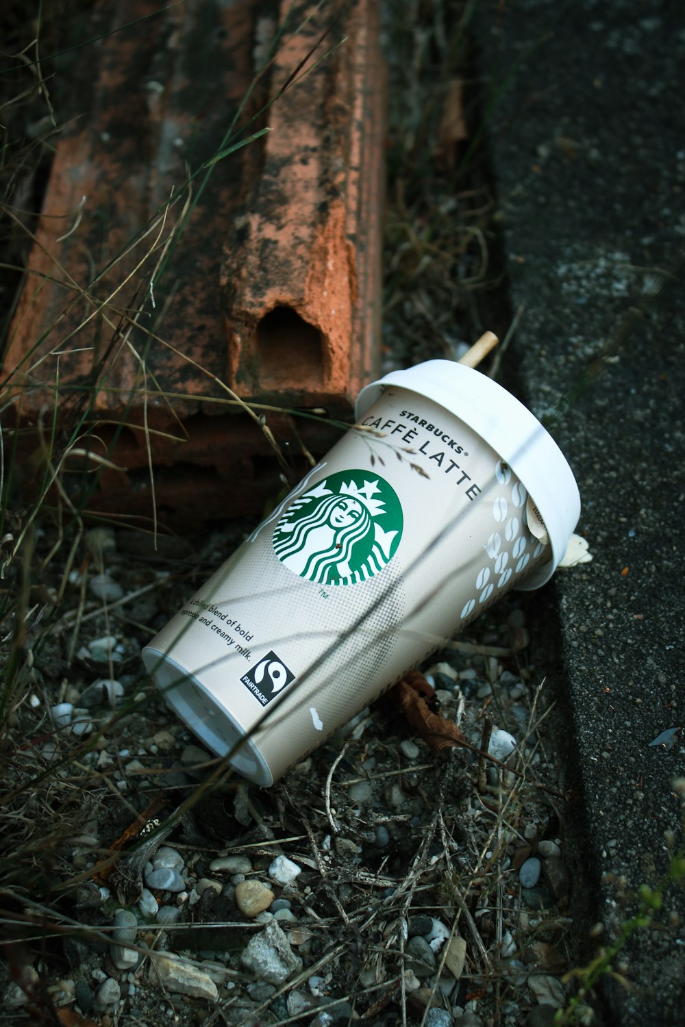 a starbucks cup sitting on the ground next to a piece of wood