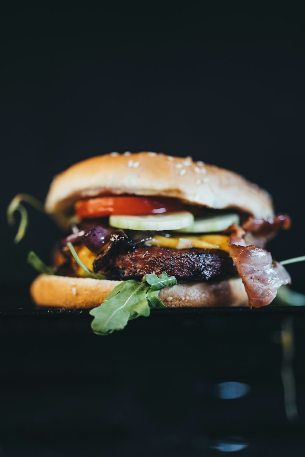 a hamburger with bacon, lettuce, tomato, and pickles