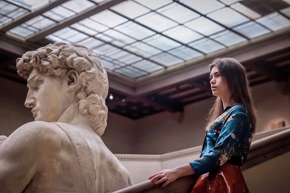 Una mujer de pie junto a una estatua de una mujer