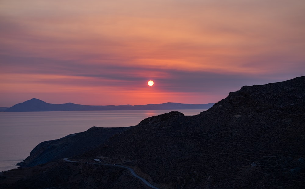 the sun is setting over the ocean and mountains