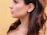 A profile of a person featuring long, dark hair and silver hoop earrings against a soft yellow background. The skin tone is smooth, and the hair slightly waves around the shoulders.