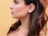 A profile of a person featuring long, dark hair and silver hoop earrings against a soft yellow background. The skin tone is smooth, and the hair slightly waves around the shoulders.