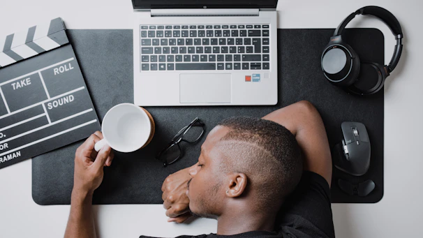 Tired woman sitting at a desk with her head in her hands, surrounded by coffee cups.
