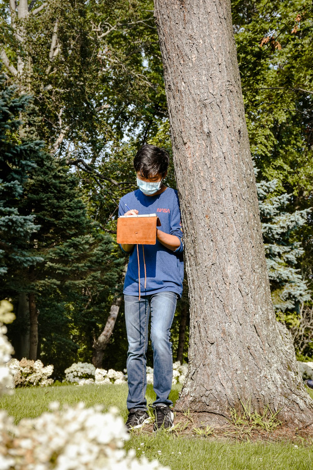 a person wearing a face mask standing next to a tree