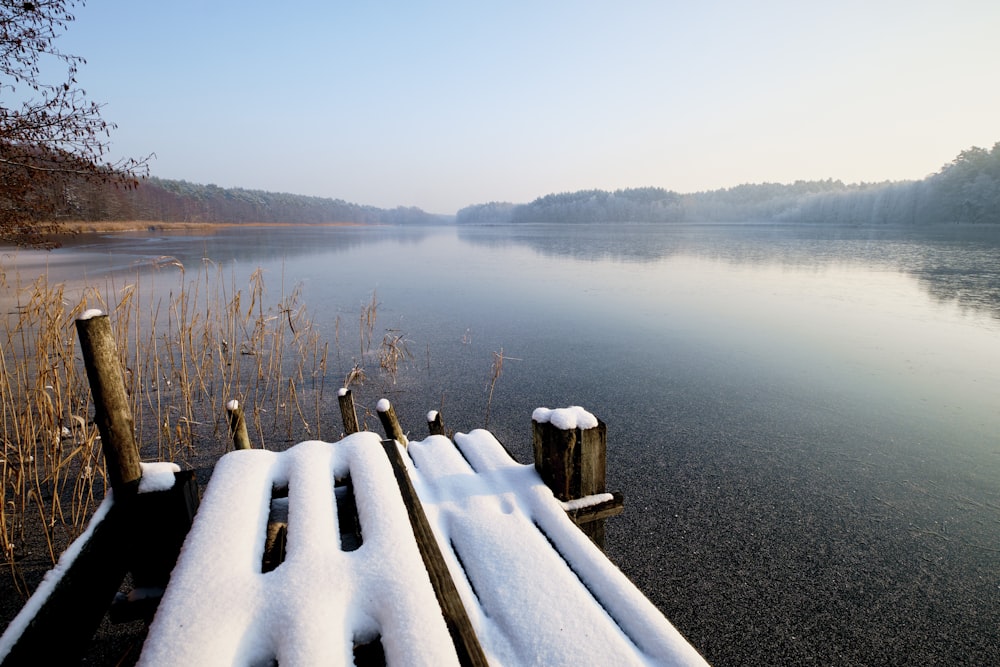a snow covered bench sitting next to a body of water