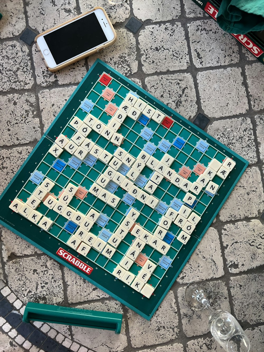 a scrabble board sitting on the ground next to a cell phone
