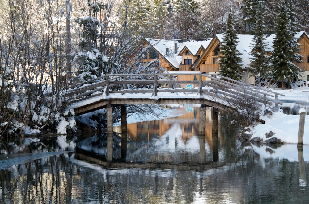 a wooden bridge over a small pond in a snow covered forest