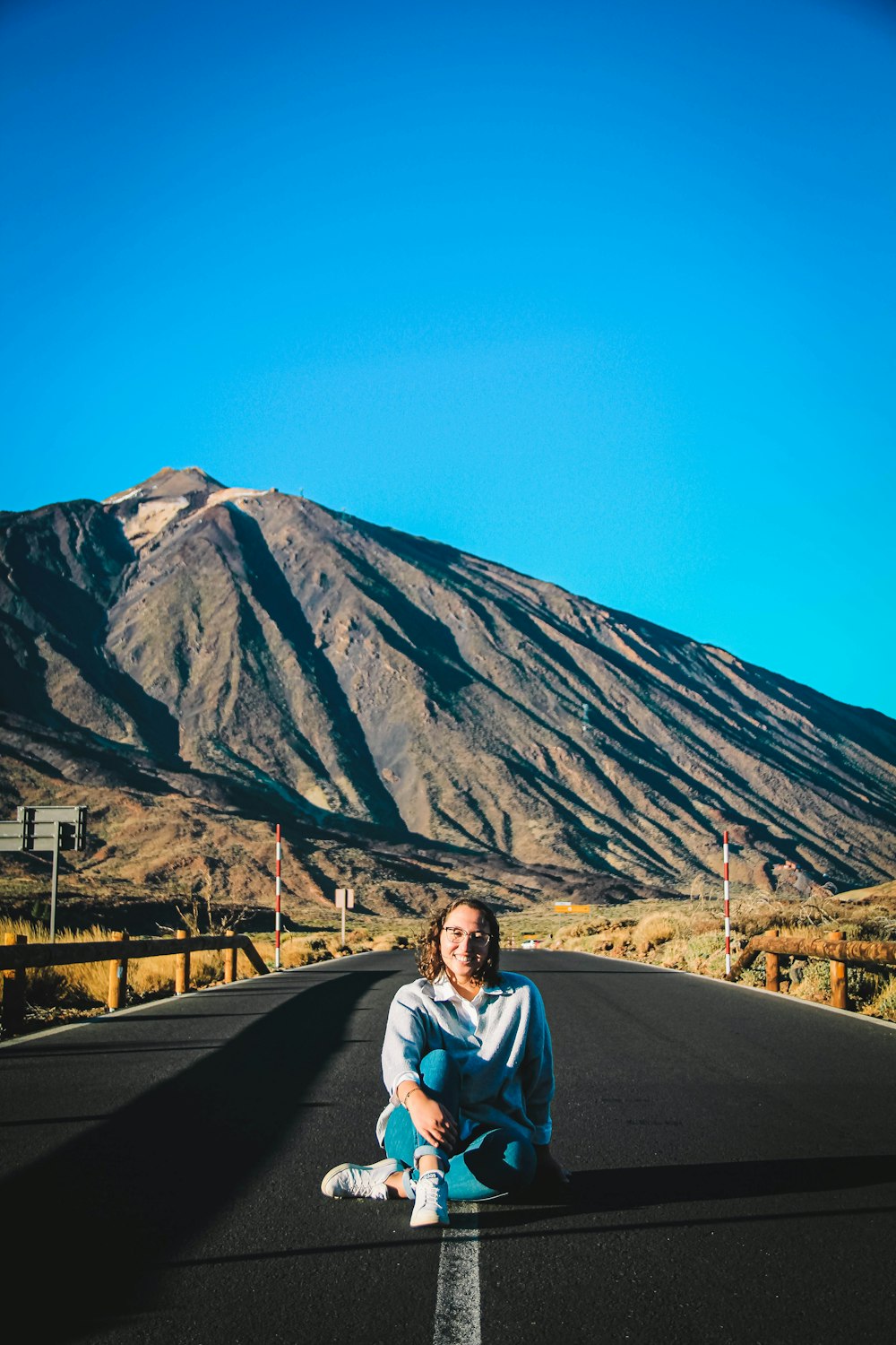a woman sitting on the side of a road in front of a mountain