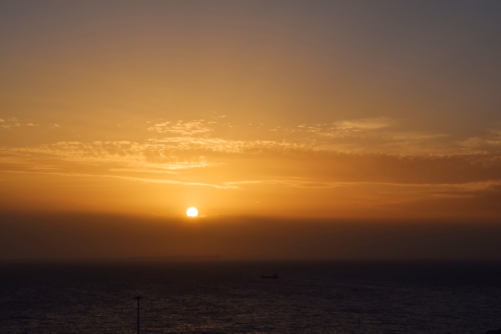 the sun is setting over the ocean with a boat in the distance