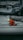 A person in a bright orange and yellow rain suit is kneeling on a white sailboat at a marina, surrounded by other boats and dock lines. The person appears to be adjusting or checking something on the deck.