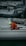 A person in a bright orange and yellow rain suit is kneeling on a white sailboat at a marina, surrounded by other boats and dock lines. The person appears to be adjusting or checking something on the deck.