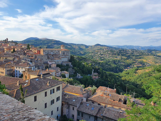 A charming Tuscan village street lined with colorful buildings and blooming flowers under a bright blue sky.