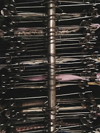 A close-up view of a metallic spiral-bound bookbinding mechanism surrounded by a stack of textile swatches. The fabrics are arranged in various colors and textures, and each swatch is clipped into the ring system to keep them in place.