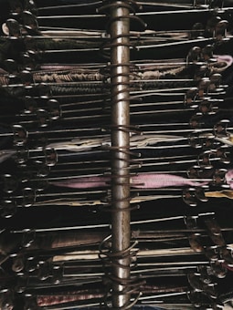 A close-up view of a metallic spiral-bound bookbinding mechanism surrounded by a stack of textile swatches. The fabrics are arranged in various colors and textures, and each swatch is clipped into the ring system to keep them in place.